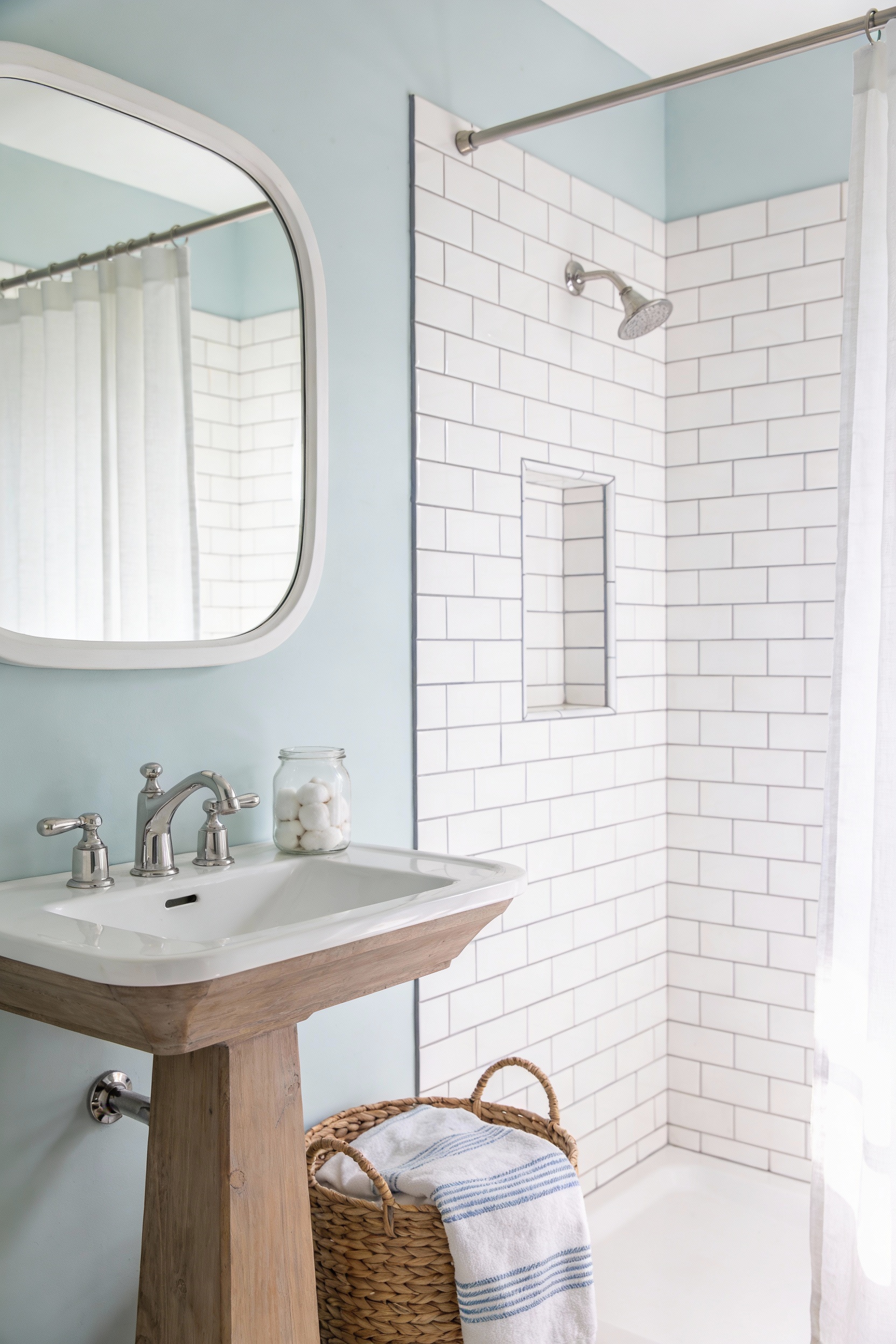 Medium photorealistic corner-angle shot of a bright coastal guest bath: soft creamy white or palest sea-salt blue walls,