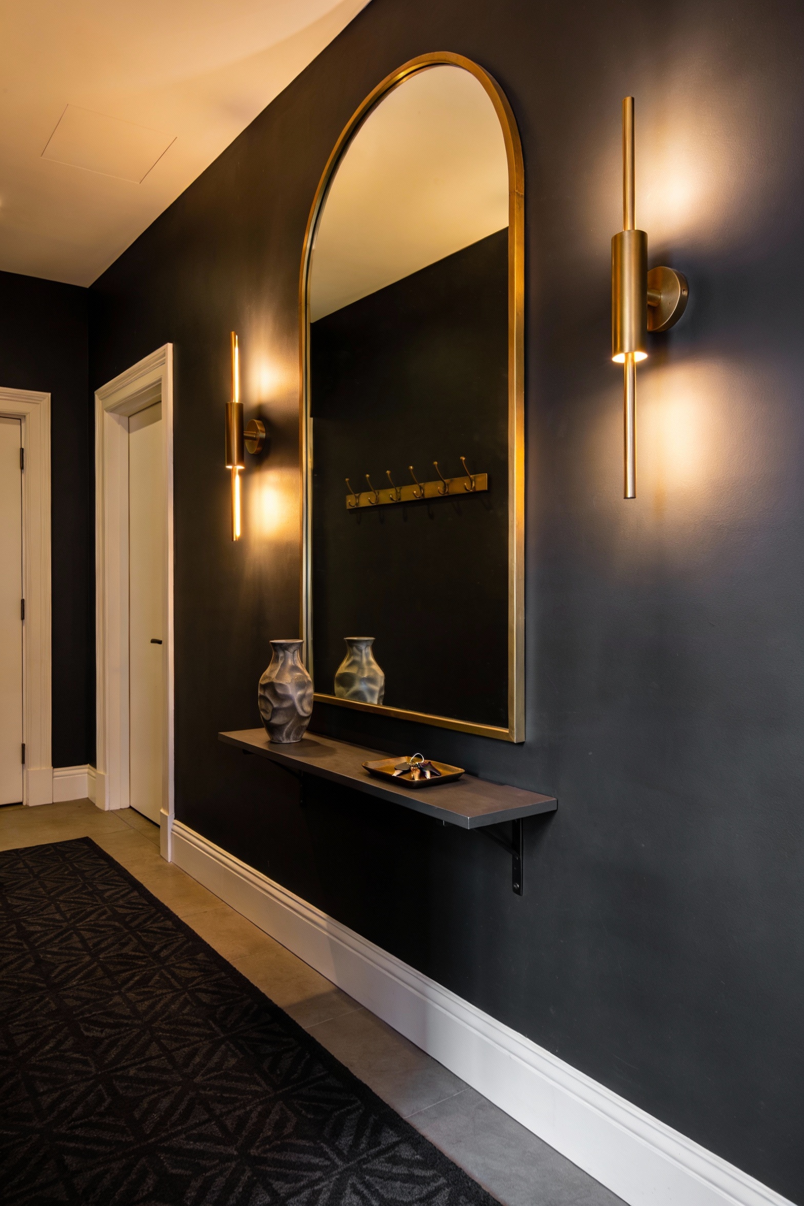 Medium corner-angle shot of a moody boutique-hotel hallway with deep charcoal/inky gray walls and crisp white trim, warm