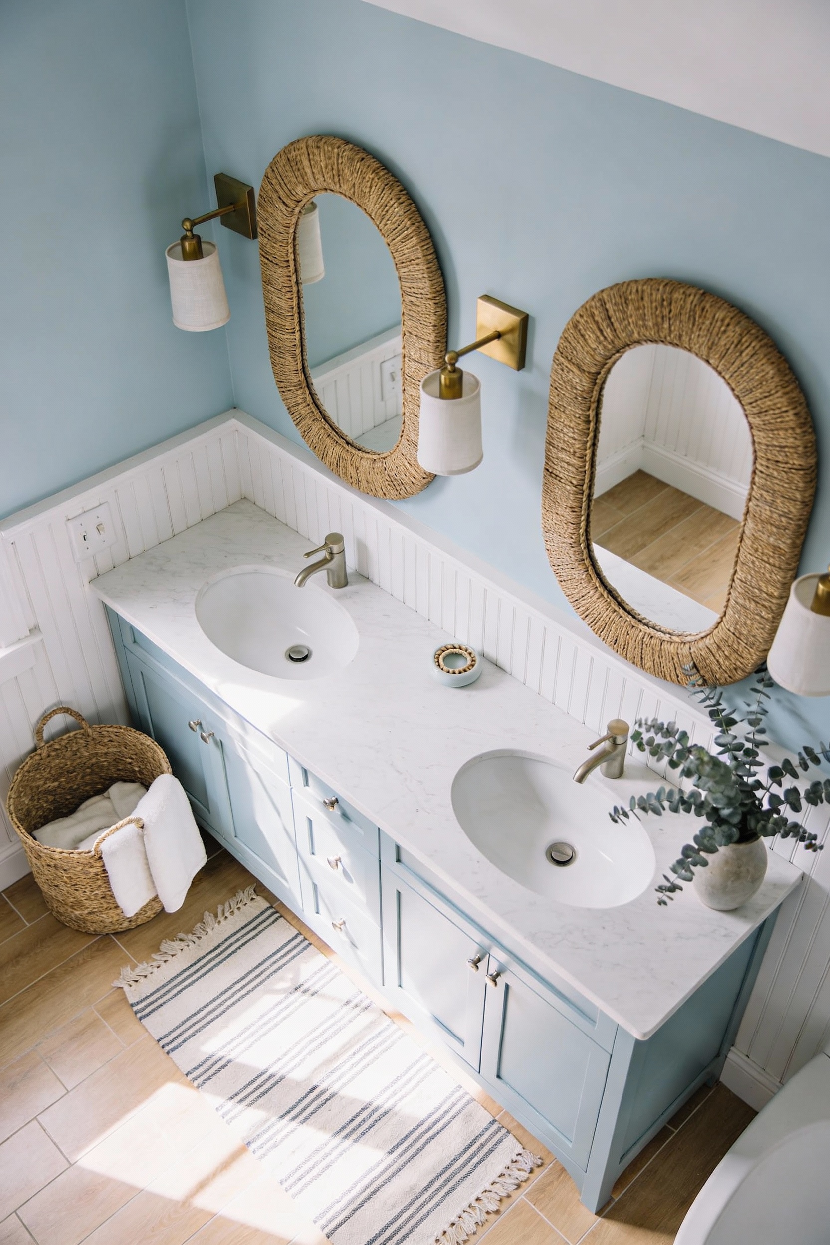 Overhead/corner angle photorealistic coastal bathroom scene: washed pale blue double vanity with soft matte finish, whit